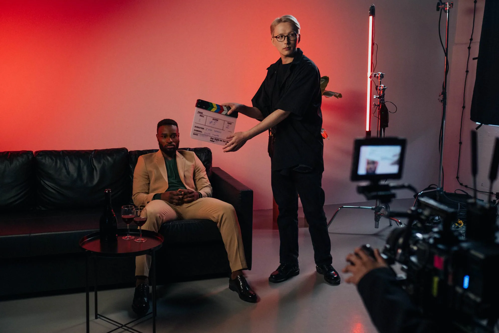 A clapperboard snapped in front of an actor on a pink-lit set