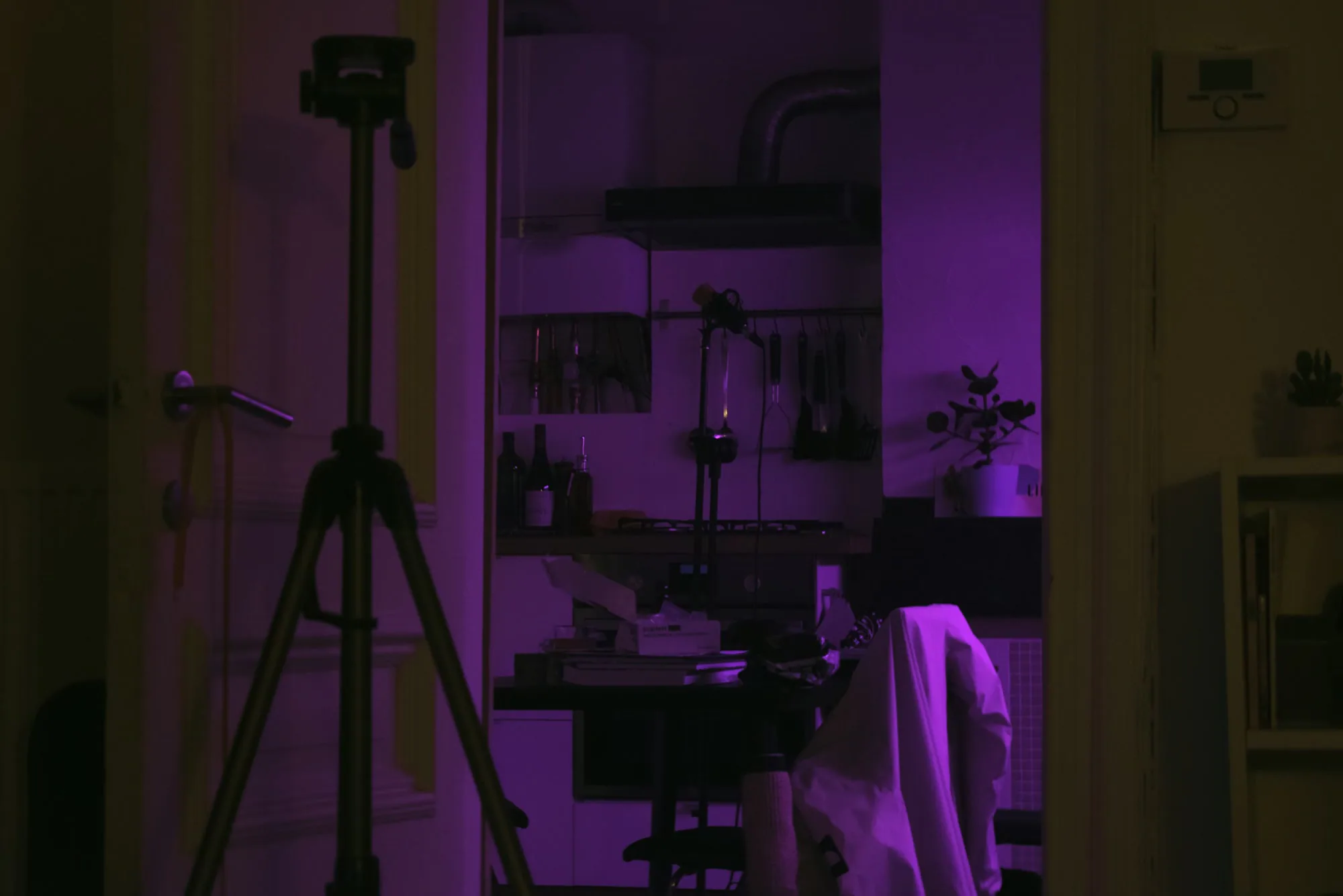 A tripod in a purple-lit apartment doorway